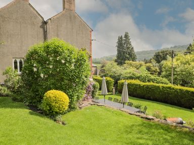 A garden with shrubs and patio furniture with umbrellas near a building at Viaduct House in Lydbrook