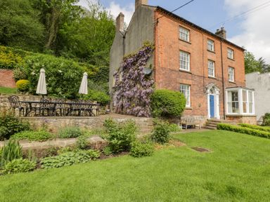 A brick house with a garden table and chairs on a patio and plants growing on the side at Viaduct House in Lydbrook