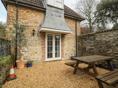 An outdoor patio area with a wooden picnic table stone walls potted plants and a door at Aldrich Cottage in Radstock