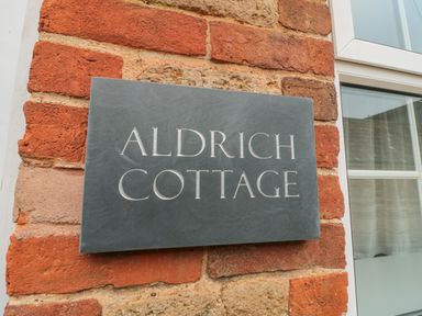 A sign reading Aldrich Cottage mounted on a brick wall next to a window at Aldrich Cottage in Radstock