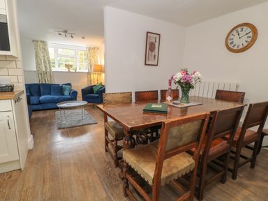 A dining area with a wooden table and eight chairs next to a living room with blue sofas and a coffee table at Aldrich Cottage in Radstock