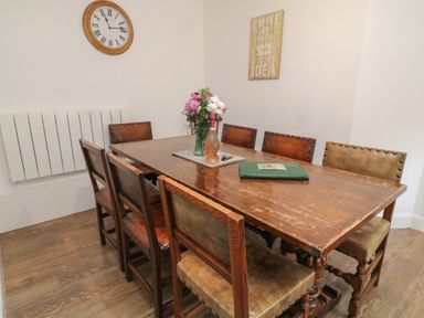 A dining room with a wooden table and chairs and a clock on the wall at Aldrich Cottage in Radstock