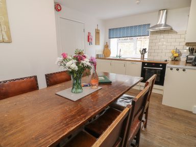 A kitchen with wooden dining table and chairs a vase with flowers on the table and kitchen appliances at Aldrich Cottage in Radstock