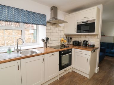 A kitchen with white cabinets wooden countertops and a blue valance over the window at Aldrich Cottage in Radstock