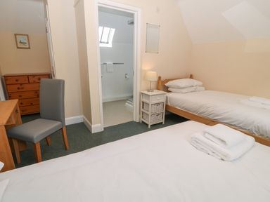 A bedroom with two single beds a wooden desk and chair a chest of drawers and an ensuite bathroom at Aldrich Cottage in Radstock