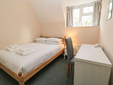 A small bedroom with a wooden bed, white bedding, folded towels, a desk with a chair and a window at Aldrich Cottage in Radstock
