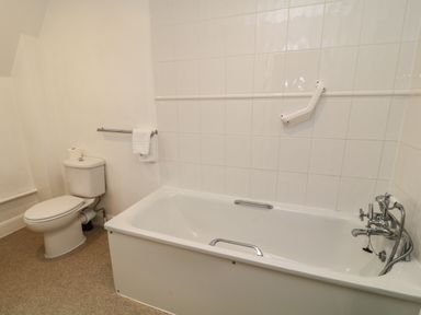 A bathroom with a toilet and a bathtub with grab bars and a towel rack at Aldrich Cottage in Radstock