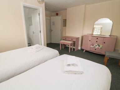 A bedroom with two single beds with white linens and towels a vanity desk with a bench a dresser with a mirror and a small stool at Aldrich Cottage in Radstock