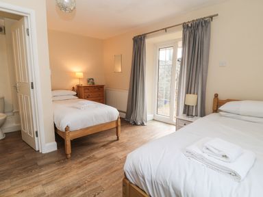 A bedroom with two single beds a wooden chest of drawers a bedside table and a door leading outside at Aldrich Cottage Radstock
