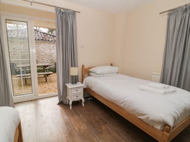 A bedroom with two single beds a bedside table with a lamp and patio doors leading outside at Aldrich Cottage in Radstock