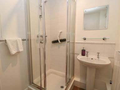 A bathroom with a corner shower enclosure a white pedestal sink a mirror and a towel on a rail at Aldrich Cottage in Radstock