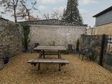 An outdoor seating area with a wooden picnic table and benches surrounded by stone walls and black chairs at Aldrich Cottage in Radstock