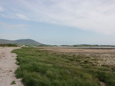 A coastal landscape with a gravel path green grass and a sandy shore with a mountain in the distance at Cheri in Southerness
