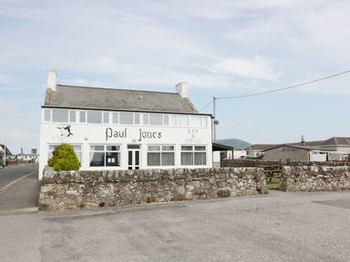 A building with Paul Jones bar and grill sign with a stone wall and a tree outside at Cheri in Southerness