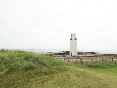 A lighthouse near a rocky shore with grass and a wooden fence at Cheri in Southerness