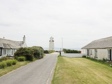 A road between two cottages leading to a lighthouse near the sea at Cheri in Southerness