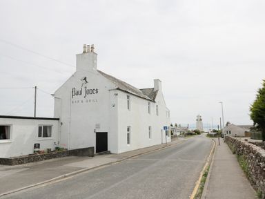 A street with a white building labeled Paul Jones Bar and Grill and a lighthouse in the distance at Cheri in Southerness