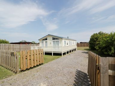A white mobile home with a porch surrounded by a wooden fence and a gravel driveway at Cheri in Southerness