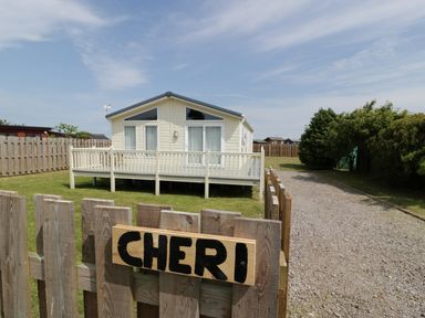 A small house with a porch behind a wooden fence with a sign that says Cheri in Southerness
