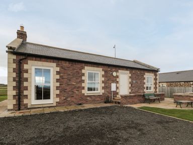 A single-story brick house with three windows and a door with a small patio area with benches at West Gate in Embleton
