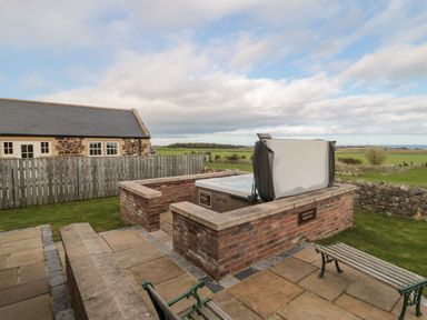An outdoor hot tub with a raised brick wall around it and benches on a patio at West Gate in Embleton