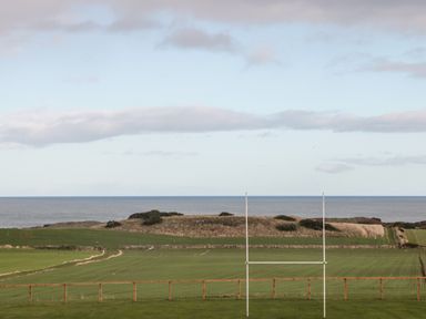 A rugby goalpost on a grassy field with hills and the sea in the background at West Gate in Embleton