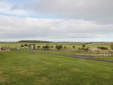 A grassy field with a playground and wooden fences at West Gate in Embleton