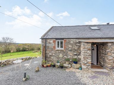 Stone cottage exterior with potted plants and outdoor seating on gravel at Celyn Farm Cottage in Deiniolen near Llanberis