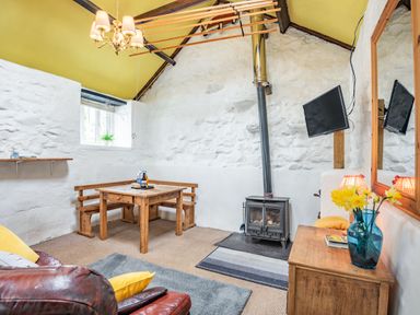 A room with a wood stove a wooden dining table with benches a mounted tv and a leather chair at Celyn Farm Cottage in Deiniolen near Llanberis