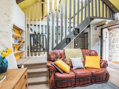 A sitting area with a brown leather sofa with yellow pillows and stairs with railing in a cottage at Celyn Farm Cottage Deiniolen near Llanberis