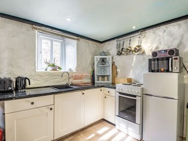 A kitchen with a stove fridge microwave toaster kettle and hanging pots at Celyn Farm Cottage Deiniolen near Llanberis