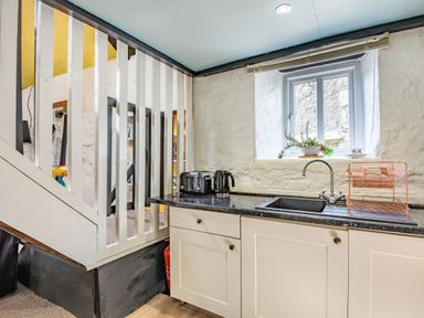 A kitchen area with a black countertop white cabinets a black sink toaster kettle dish rack and a small window at Celyn Farm Cottage in Deiniolen near Llanberis