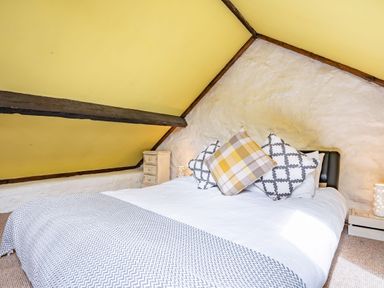 A bedroom with a bed and pillows under a sloped yellow ceiling at Celyn Farm Cottage Deiniolen near Llanberis
