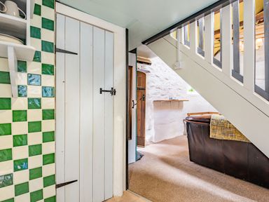 A staircase next to a brown leather sofa and a wooden door in a room with white stone walls at Celyn Farm Cottage in Deiniolen near Llanberis