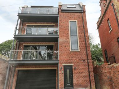 A red brick building with three balconies and a black door at The Office Gardens Apartment 2 Whitby