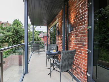 A balcony with two tables and four chairs overlooking trees and brick walls at The Office Gardens Apartment 2 in Whitby