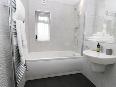 A bathroom with a bathtub shower combination a sink and towels on a rack at The Office Gardens Apartment 2 in Whitby