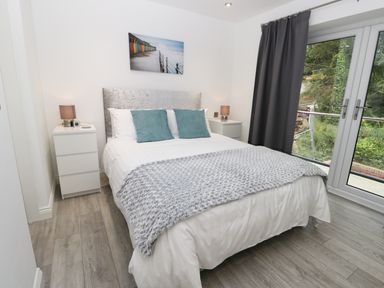 A bedroom with a double bed two teal pillows two bedside tables with lamps and a large window with dark curtains at The Office Gardens Apartment 2 in Whitby