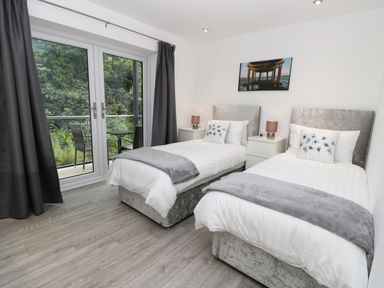 A bedroom with two single beds bedside tables and lamps next to doors leading to a balcony at The Office Gardens Apartment 2 in Whitby