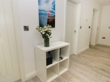A white storage unit with a vase of white flowers on top and wall art above at The Office Gardens Apartment 2 in Whitby