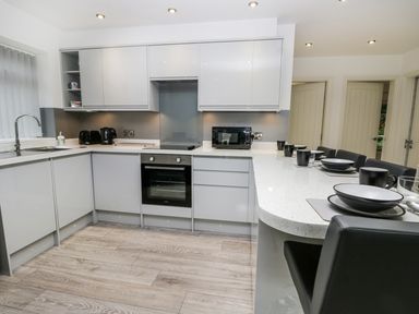 A kitchen with grey cabinets a built-in oven a microwave toaster kettle and a counter with black chairs and place settings at The Office Gardens Apartment 2 Whitby