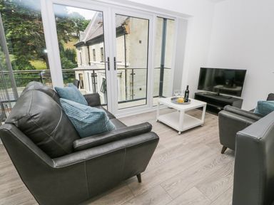 A living room with two black sofas a white coffee table and a TV at The Office Gardens Apartment 2 in Whitby