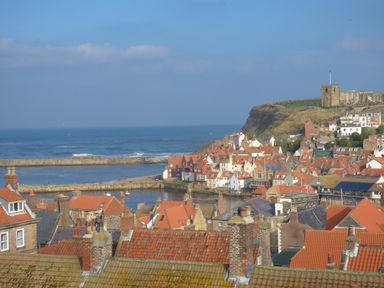 A coastal town with red tiled roofs and a stone church on a hill by the sea at The Office Gardens Apartment 2 in Whitby