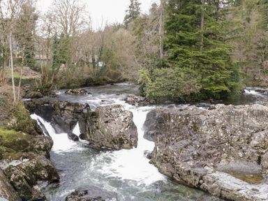 A river flowing over rocks with trees surrounding the area at Dale Cottage in Llanrwst