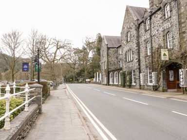 A street with a stone building marked Royal Oak Hotel and a sidewalk with trees and parking at Dale Cottage in Llanrwst