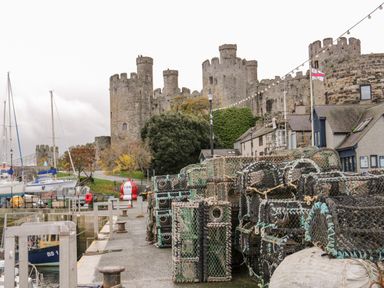 A harbor scene with fishing equipment stacked on the dock and a castle in the background at Dale Cottage in Llanrwst