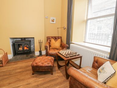 A sitting area with two leather chairs a footstool and a chessboard on a wooden table by a fireplace at Dale Cottage in Llanrwst