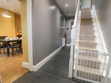 A hallway with tiled floor a staircase with carpet and baby gate and a dining area with table and chairs at Dale Cottage in Llanrwst