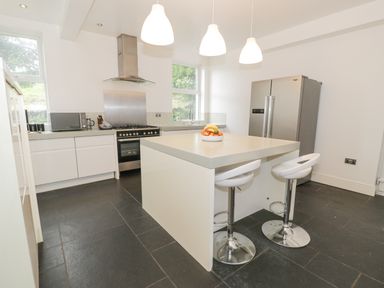 A kitchen with a white island with stools a stainless steel stove and fridge at Dale Cottage in Llanrwst
