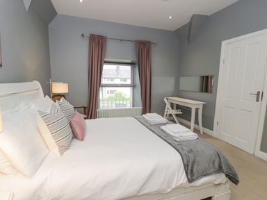 A bedroom with a bed pillows and folded towels a desk with a chair a window with curtains at Dale Cottage in Llanrwst
